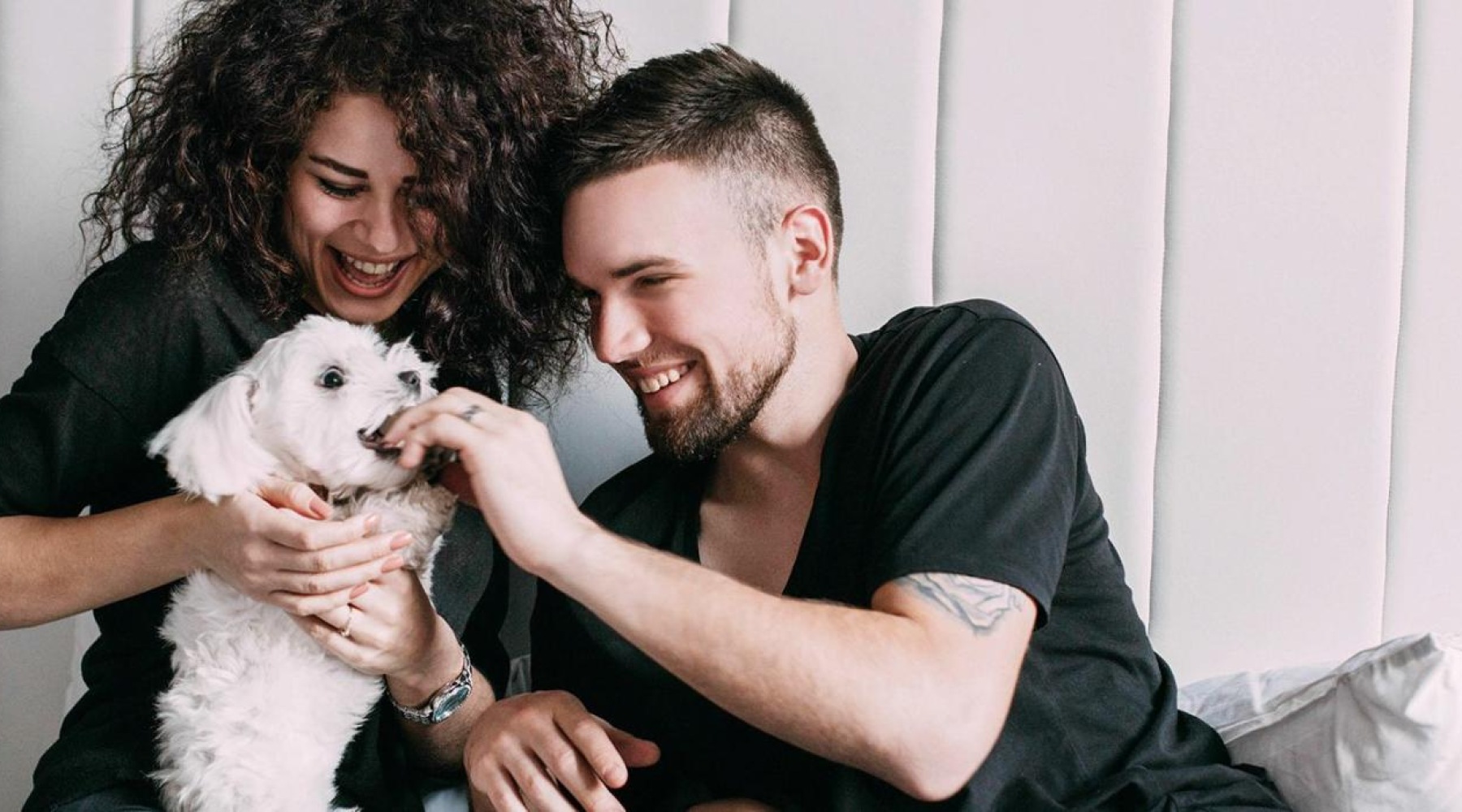 a man and woman sitting on a bed playing with a dog